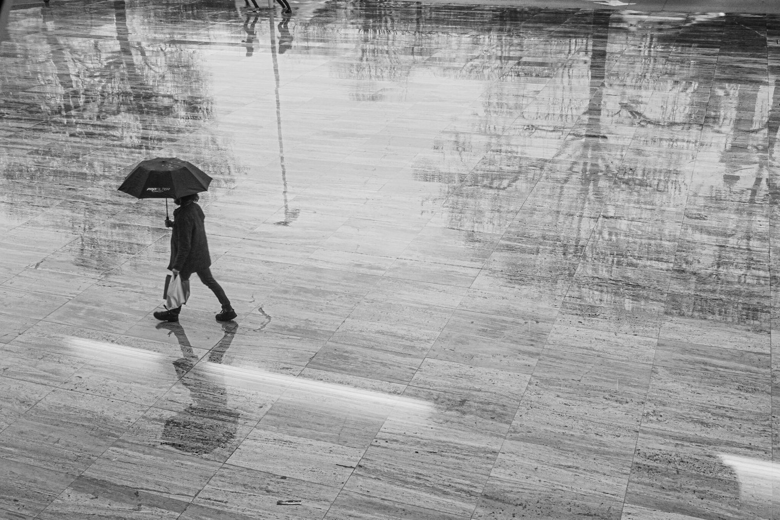 A person crossing wet paving under an umbrella during Porto's rainy winter season