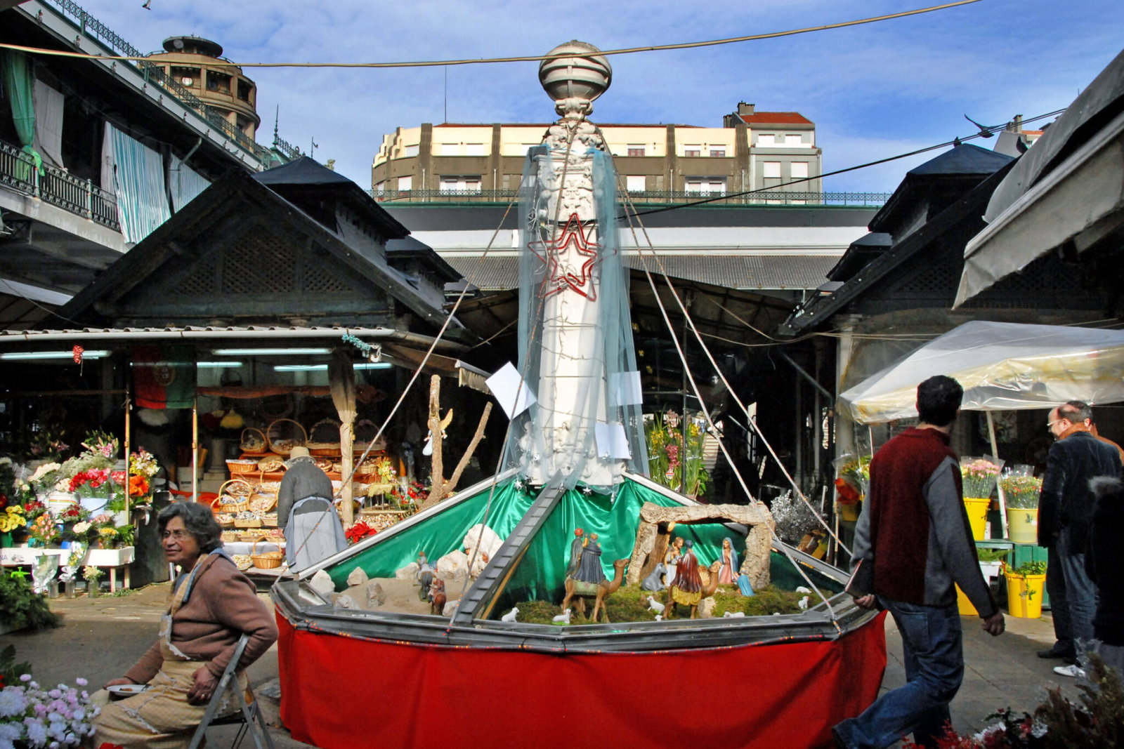 Une crèche de Noël installée autour de la fontaine à l’intérieur du Mercado do Bolhão à Porto, avec des étals de fleurs à l’arrière-plan
