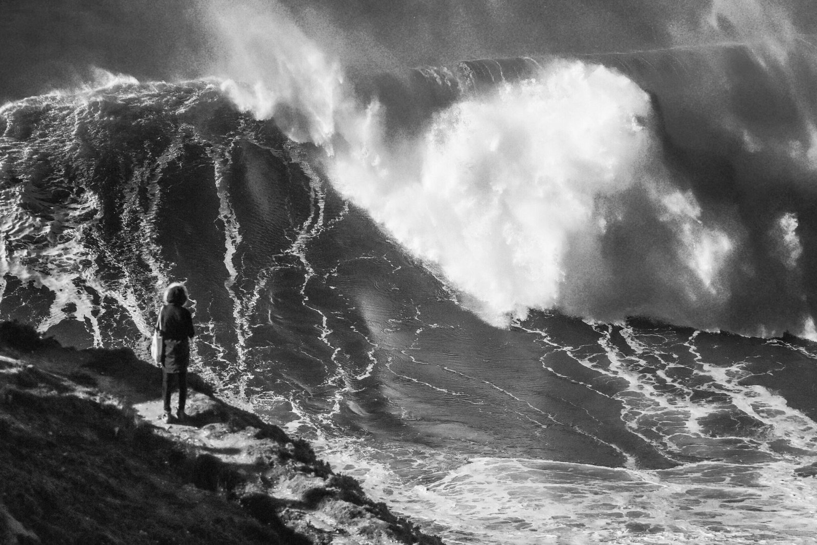 A spectator on the cliff watching a giant wave break at Praia do Norte in Nazare
