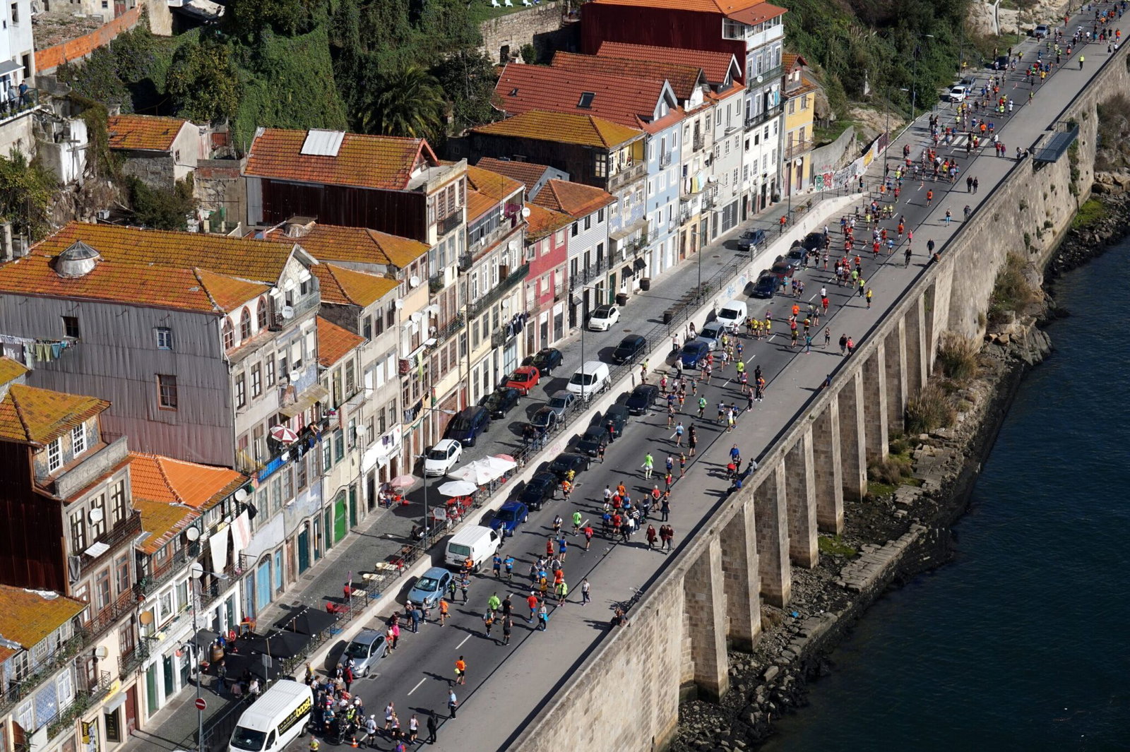 Porto Marathon runners on the riverside road beside the Douro, seen from above with the old town houses alongside