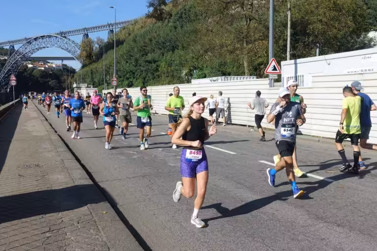 Runners in the Porto Marathon on the riverside road along the Douro, with the Maria Pia bridge behind